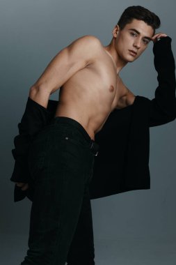 Pantolonlu çıplak bir adam ve gri arka planda bir ceket yana eğilmiş.