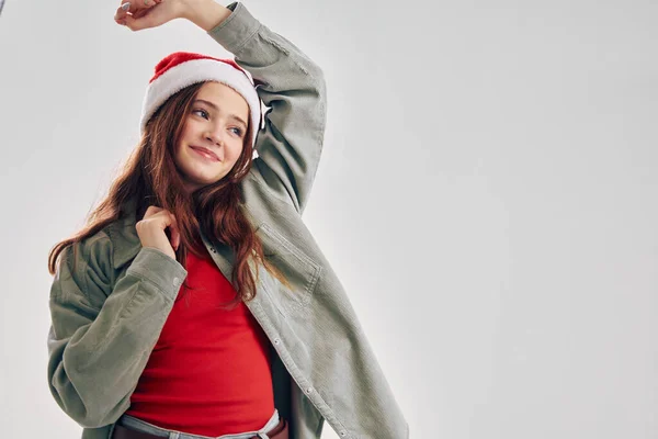 Joyeuse petite fille gesticulant avec ses mains sur un fond gris et santa claus coiffe cadeaux de vacances — Photo