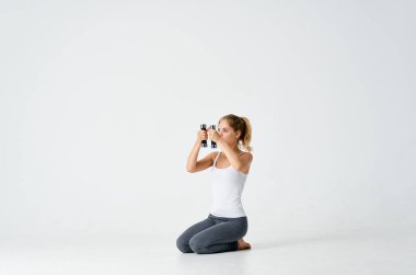 Elinde dambıllar olan spor bir kadın yerde oturuyor.