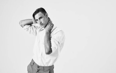 Hafif arka planda pantolon ve gömlek giymiş genç bir adam elleriyle kafasına dokunuyor.