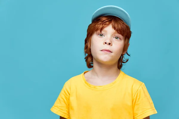 Рыжий мальчик с удивленным выражением лица синяя кепка желтая футболка синий фон — стоковое фото