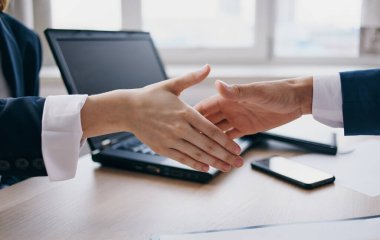 İş yerindeki çalışanlar masada el sıkışıyor ve arka planda bir laptop var.