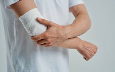 Kolu bandajlı, dirseği ve parmağı yaralı bir adam.