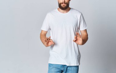 Beyaz tişörtlü, arka planda jestler yapan, elleri kesilmiş, kot pantolonlu bir adam mekanı taklit ediyor.