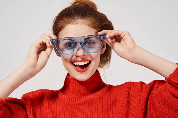 Mooie vrouw in een rode trui met blauwe bril op een lichte achtergrond — Stockfoto