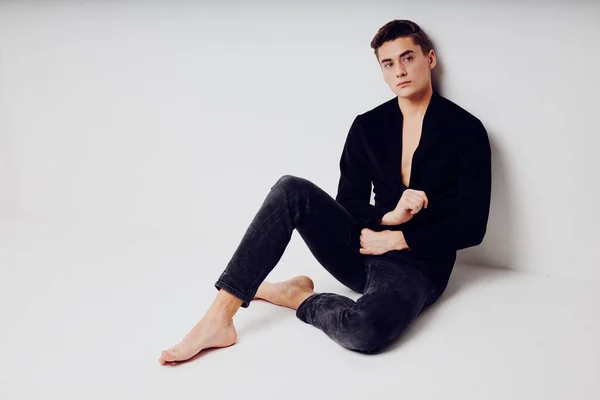 Um homem bonito está sentado no chão em uma jaqueta de estilo moderno preto — Fotografia de Stock
