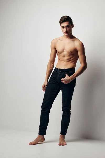 A sexy guy with a naked torso and in trousers is standing barefoot on the floor in a room — Stock Photo, Image