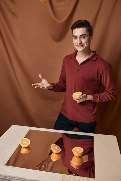 Όμορφος άντρας στέκεται δίπλα στο τραπέζι με έναν καθρέφτη με πορτοκάλια — Φωτογραφία Αρχείου