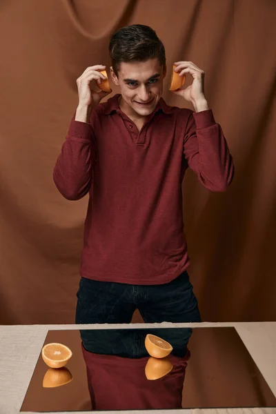 Hombre guapo peinado de moda espejo en la mesa naranjas en las manos — Foto de Stock