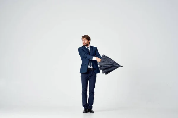 Homem de negócios em um terno posando em um fundo claro com um guarda-chuva preto em sua mão — Fotografia de Stock