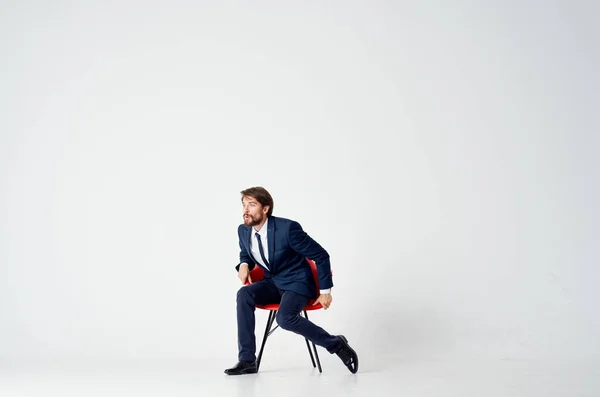 Hombre de negocios se sienta en sillas rojas en el interior y gestos con las manos sobre un fondo claro —  Fotos de Stock