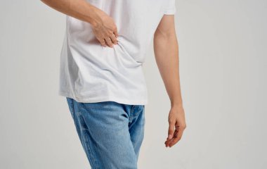 Tişörtlü ve kot pantolonlu bir adam ellerine karnına dokunuyor. Karın ağrısı, apandisit sorunları.
