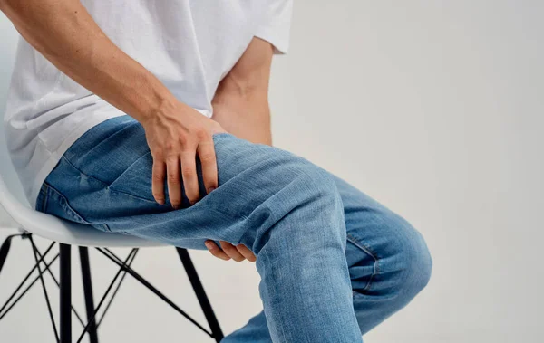 Il ragazzo si tocca la gamba con le mani su uno sfondo leggero dolore al ginocchio — Foto Stock