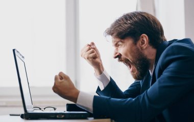 İş adamı, dizüstü bilgisayarın önünde takım elbiseyle masada oturuyor.