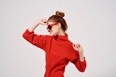 Hafif arka planda güneş gözlüklü şık bir kadın ve kırmızı kazak modeli makyajı.