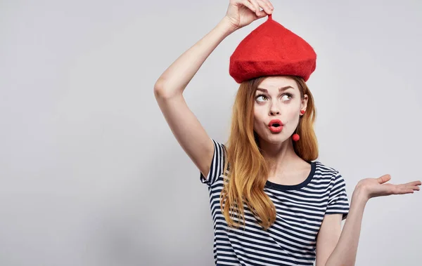 Donna in t-shirt a righe tocca cappello rosso sulla sua testa luce sfondo vista ritagliata — Foto Stock