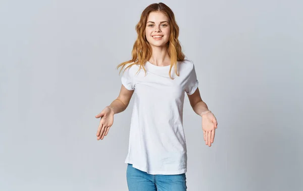 Hermosa mujer en una camiseta blanca y pantalones vaqueros sobre un fondo gris gestos Copiar espacio — Foto de Stock