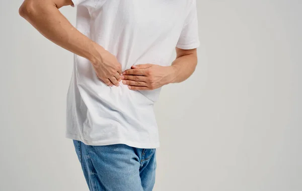 Um cara em uma camiseta e jeans toca suas mãos perto do abdômen apendicite dor — Fotografia de Stock