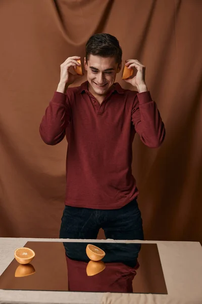 Un hombre con una camisa roja con naranjas en las manos un espejo sobre la mesa — Foto de Stock