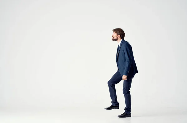 Uomo d'affari in un abito blu si trova su una gamba su uno sfondo leggero vista laterale — Foto Stock