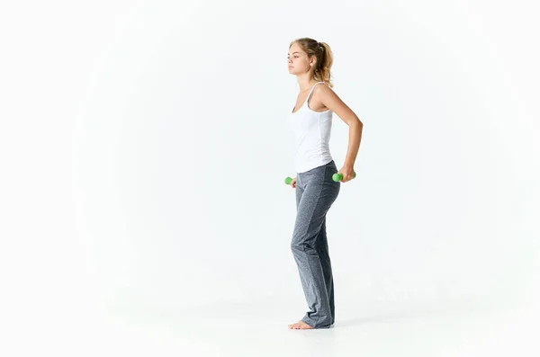 Žena jde do sportu s činkami v světlé místnosti a šedé kalhoty — Stock fotografie