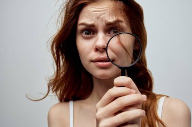 Saçları dökülmüş güzel bir kadın, ellerinde büyüteç var.