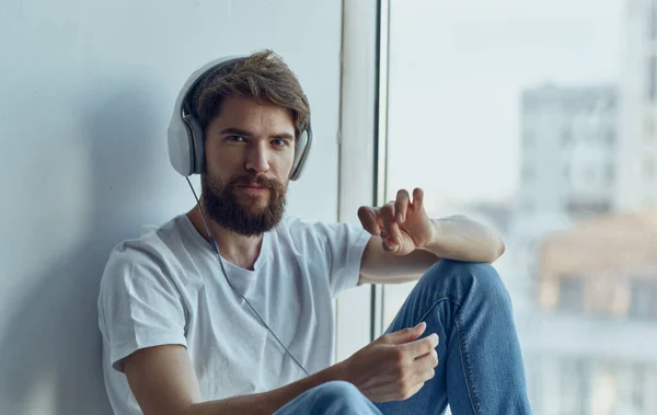 a man in headphones sits on the windowsill and listens to music imitation driving a car steering wheel Studio