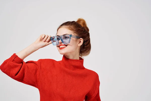 Portrait of a beautiful woman in a red sweater and blue glasses on a light background — Stock Photo, Image