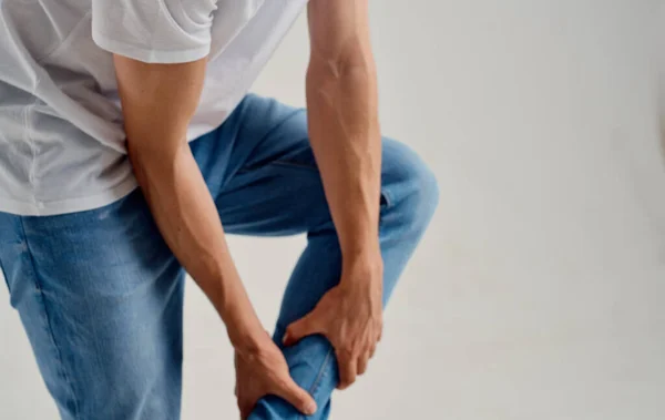 Der Kerl berührt sein Bein mit den Händen auf einem leichten Hintergrund Knieschmerzen — Stockfoto
