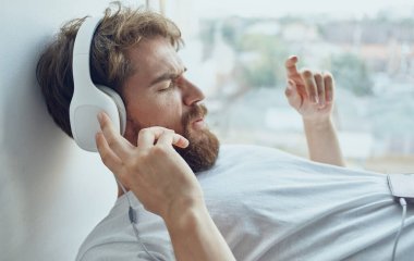 Kulaklıklı bir adam pencere kenarında müzik dinliyor.