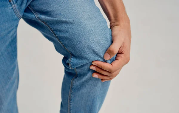 El tipo toca su pierna con sus manos sobre un ligero dolor de rodilla de fondo — Foto de Stock