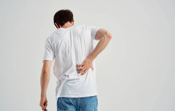 Мужчина в белой футболке прикасается к спине болью в спине — стоковое фото
