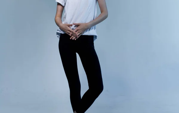 Μια γυναίκα με λευκό μπλουζάκι και μαύρα κολάν σε ένα ελαφρύ φόντο χειρονομίες με τα χέρια της περικοπεί άποψη — Φωτογραφία Αρχείου