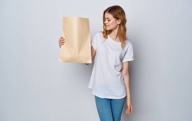 Beyaz tişörtlü ve kotlu bir kadın elinde paketle markete gidiyor.