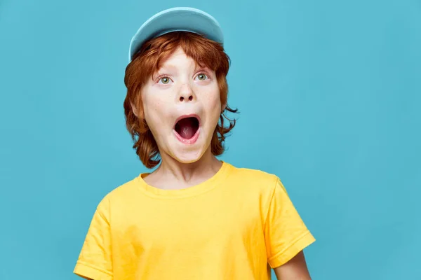 Sorprendido chico pelirrojo con la boca abierta mirando hacia arriba amarillo camiseta gorra en su cabeza —  Fotos de Stock