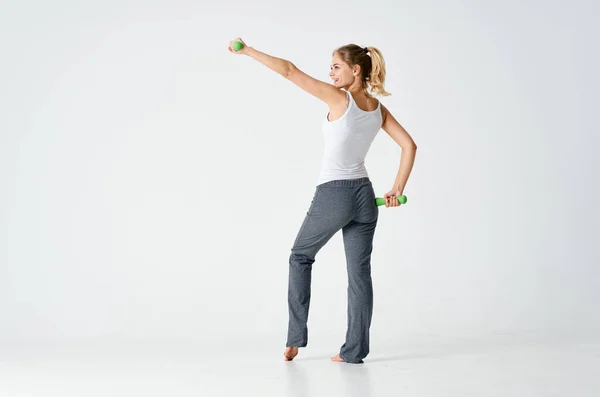 Жінка займається спортом з гантелями в світлій кімнаті і сірих штанах — стокове фото