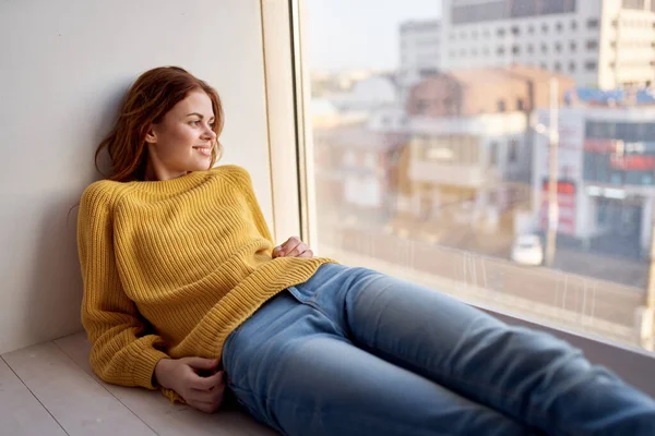 Mulher no peitoril da janela em um suéter amarelo e jeans estilo de vida de lazer — Fotografia de Stock