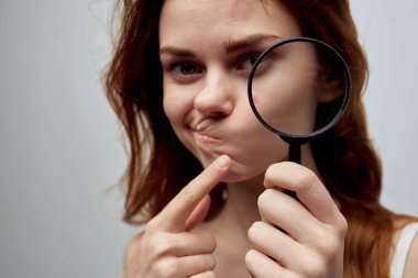 Saçları dökülmüş güzel bir kadın, ellerinde büyüteç var.