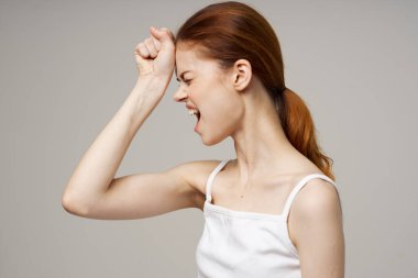 Beyaz tişörtlü güzel bir kadın yüzüne dokunuyor, elleri gri arka planda, sağlık sorunları baş ağrısı çekiyor.