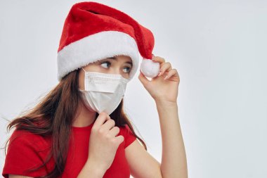 Tıbbi maske takan ve elinde Noel Baba şapkası olan bir kız. Kırmızı tişörtlü.