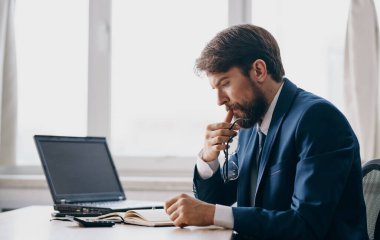 Klasik takım elbiseli bir adam masada oturur ve bir dizüstü bilgisayar ofis penceresi açık, şaşkın bir bakış.