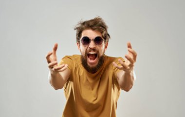 Sarı tişört gözlüklü, elleri gri arka planda duygusal bir adam.