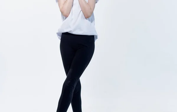 Una mujer con una camiseta blanca y polainas negras sobre un fondo claro gestos con las manos recortadas — Foto de Stock
