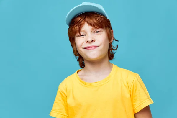 redhead boy boy with a grin on his face blue cap yellow t-shirt planning something bad