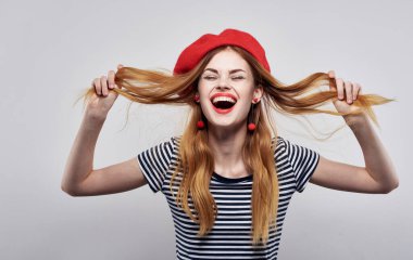 Kırmızı şapkalı ve çizgili tişörtlü mutlu bir manken. Arka planda hafif bir duygu portresi.