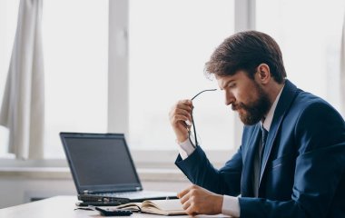 Klasik takım elbiseli bir adam masada oturur ve bir dizüstü bilgisayar ofis penceresi açık, şaşkın bir bakış.