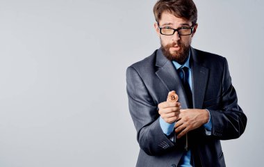 Elinde bozuk para ve gri arka planda ceketi olan bir işadamı elleriyle el kol hareketi yapıyor. 