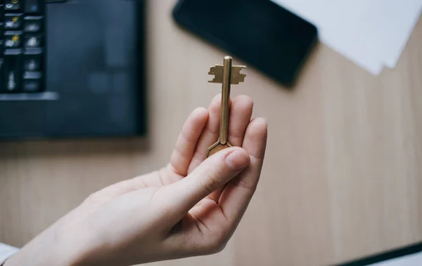 De sleutel in de hand van een vrouw in het kantoor aan tafel — Stockfoto