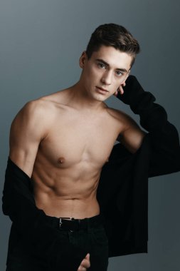 Gri arka planda çıplak bir gövdesi olan düğmesiz ceketli şık bir adam.