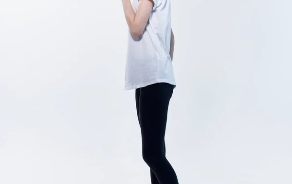 Обрезанный вид женщины в белой футболке и черных леггинсах на светлом фоне — стоковое фото